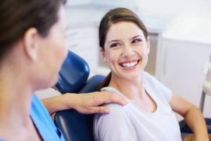 Smiling woman in a dental chair speaking with a clinician, illustrating a positive patient experience in a modern dental practice.
